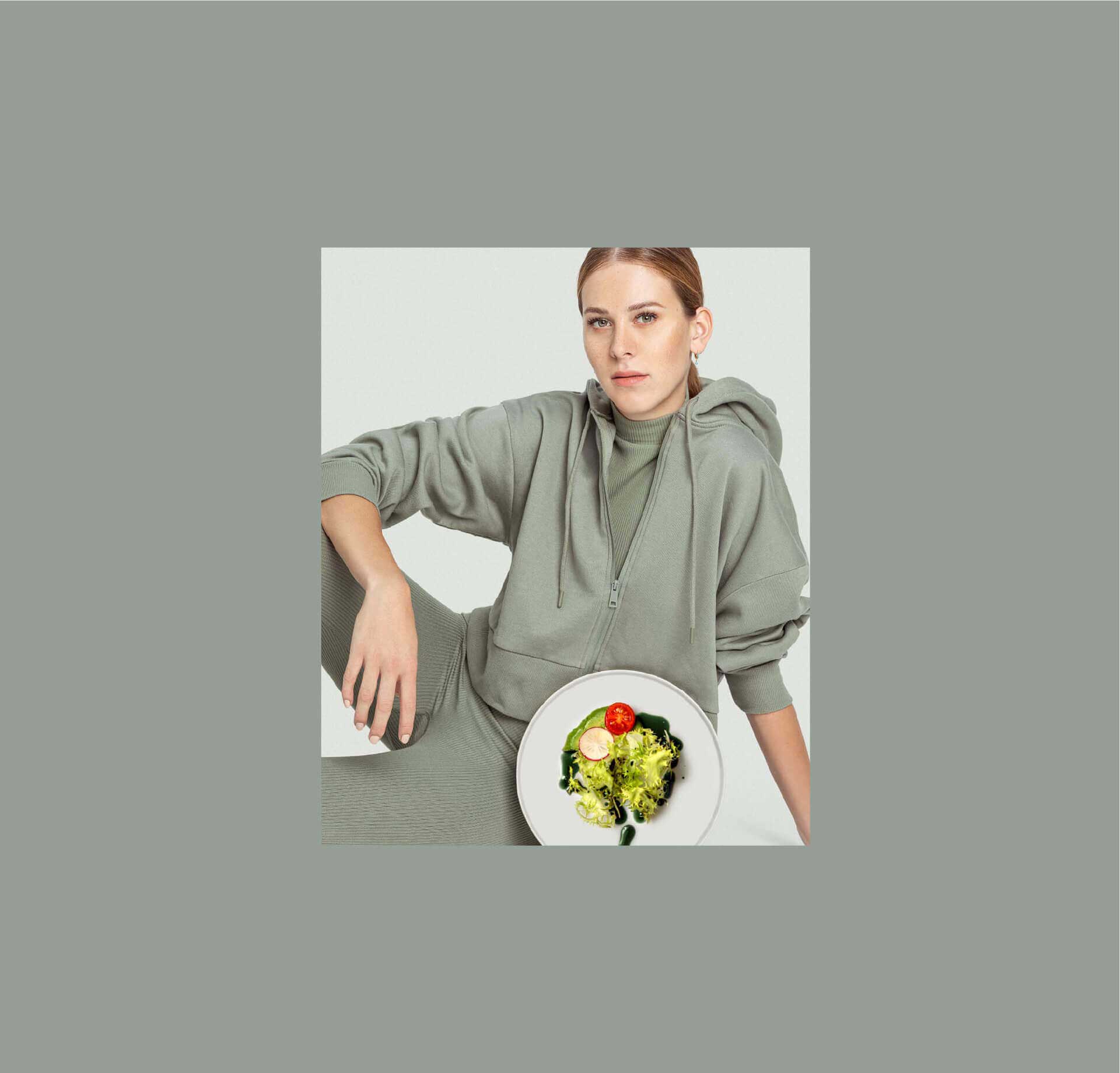 Eine Frau in einem grünen Hoodie sitzt mit einem Teller Salat vor sich , der mit original steirischem Pelzmann Kürbiskernöl garniert ist. Der Hintergrund ist neutral.